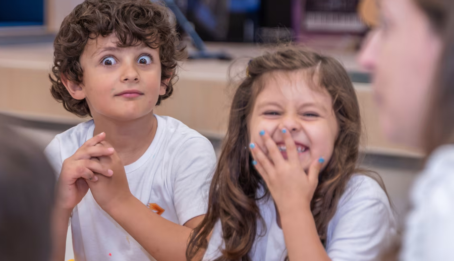 Duas crianças rindo e fazendo careta, um menino com olhos arregalados e uma menina gargalhando.