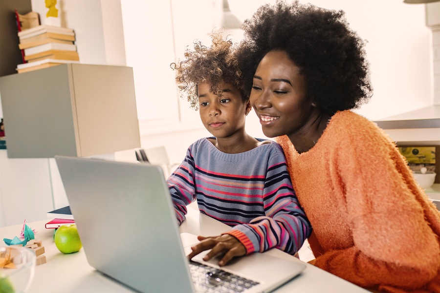 Mãe e filha afro-brasileiras aprendendo e usando um laptop em casa.