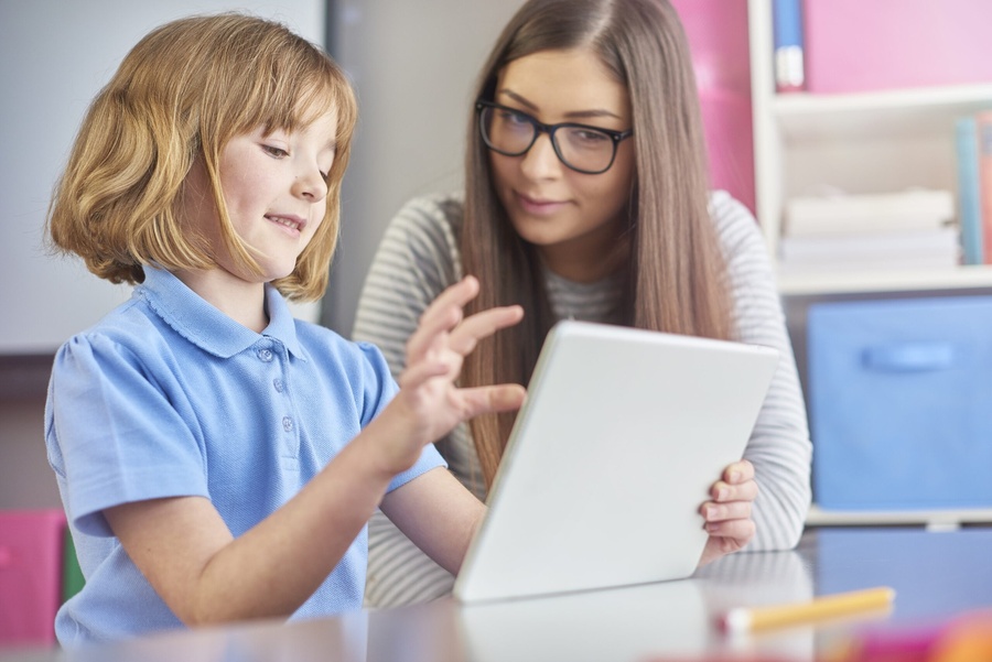 Menina e mulher usando tablet juntas em ambiente educacional.