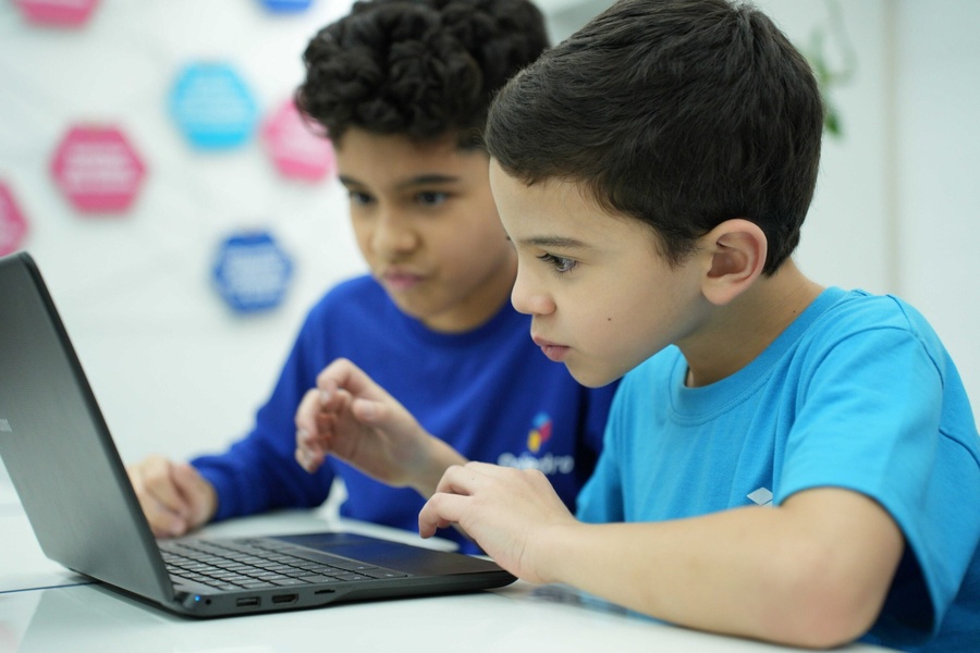 Duas crianças concentradas aprendendo e interagindo com um laptop em sala de aula.