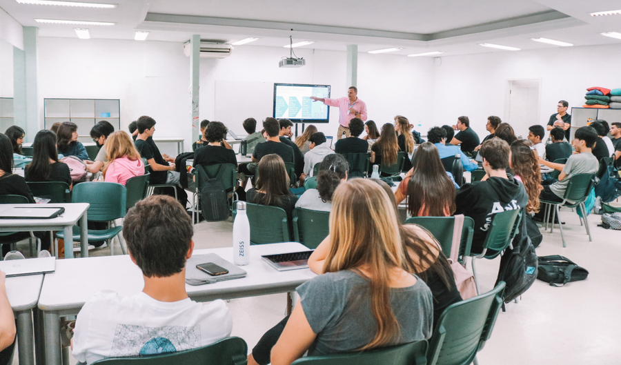 Professor de pé em sala de aula, ensinando estudantes sentados com notebooks.