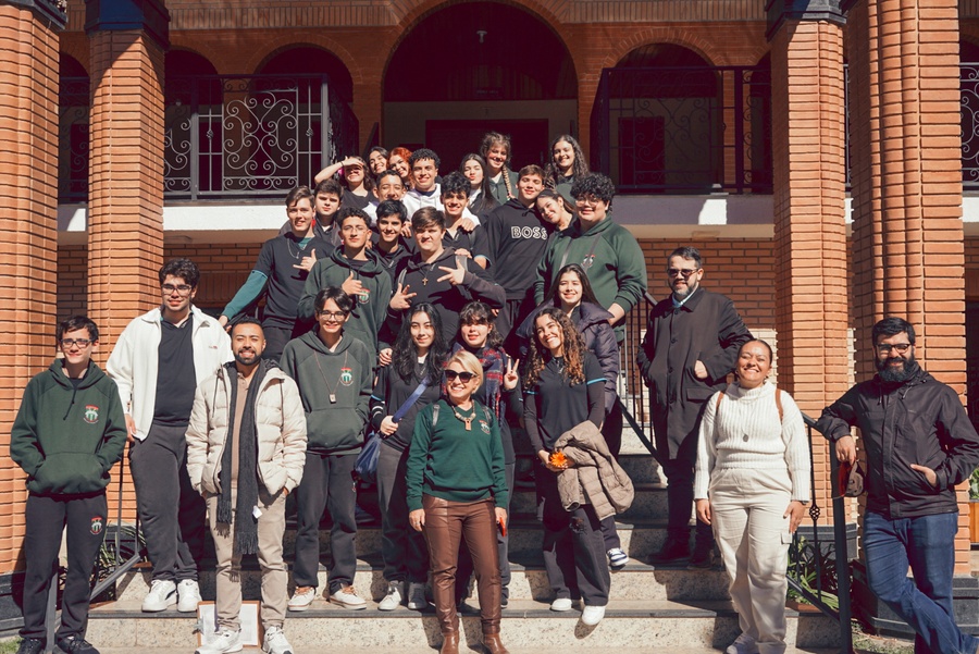 Grupo diverso de estudantes e adultos posando felizmente em escadaria de prédio de tijolos.