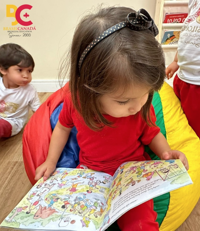 Criança lendo livro infantil ilustrado colorido sentada em pufe vibrante.