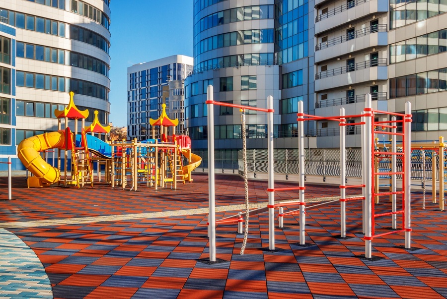 Parque infantil moderno e colorido com escorregadores e estruturas de escalada, rodeado por prédios altos.