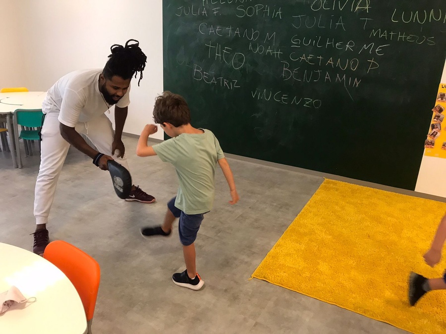 Homem segura almofada de treino para menino praticando chute em aula de artes marciais.