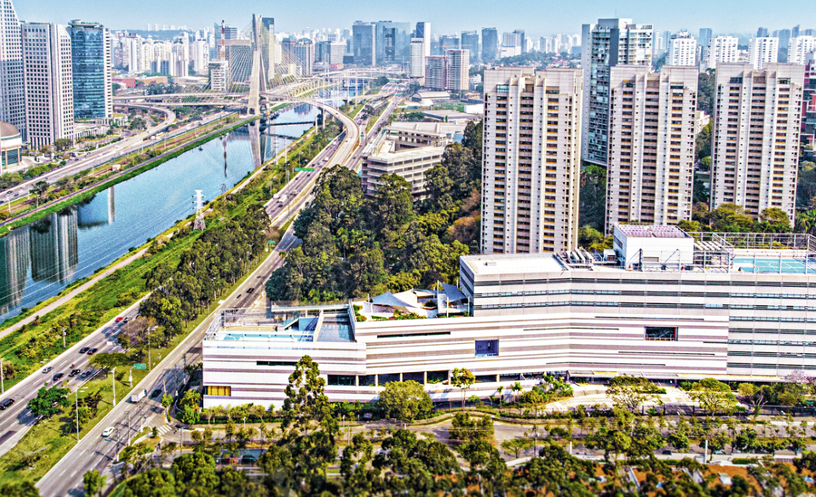 Vista aérea de cidade grande com rio, pontes, avenidas, prédios e áreas verdes.