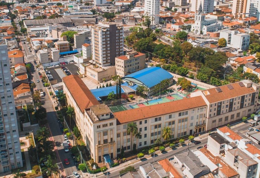Vista aérea de bairro urbano com complexo de edifícios, quadras esportivas e telhado azul.